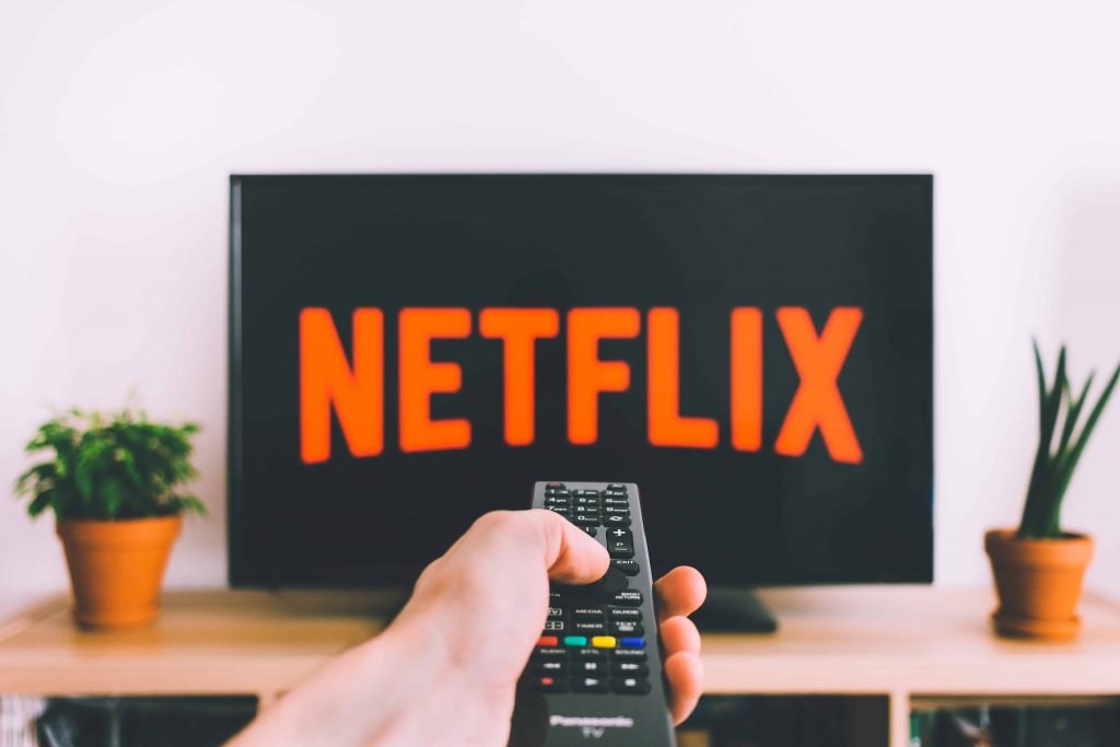 person holding remote and pointing it at a television that has the Netflix logo on display