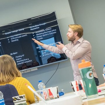 A director presenting to a group pointing at a TV