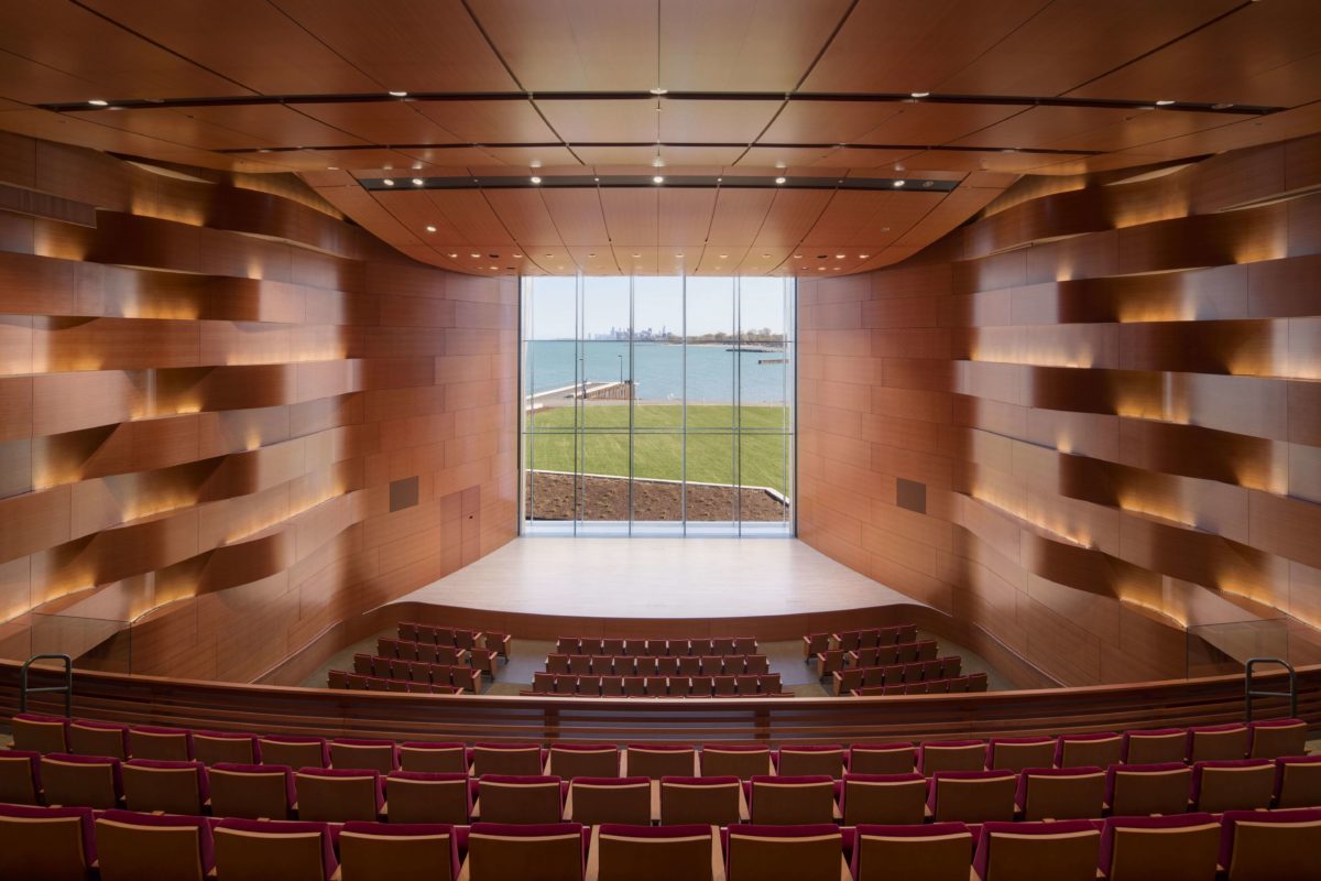 Empty indoor concert venue, from the seats, looking at the stage that has a large window to a lake view behind it