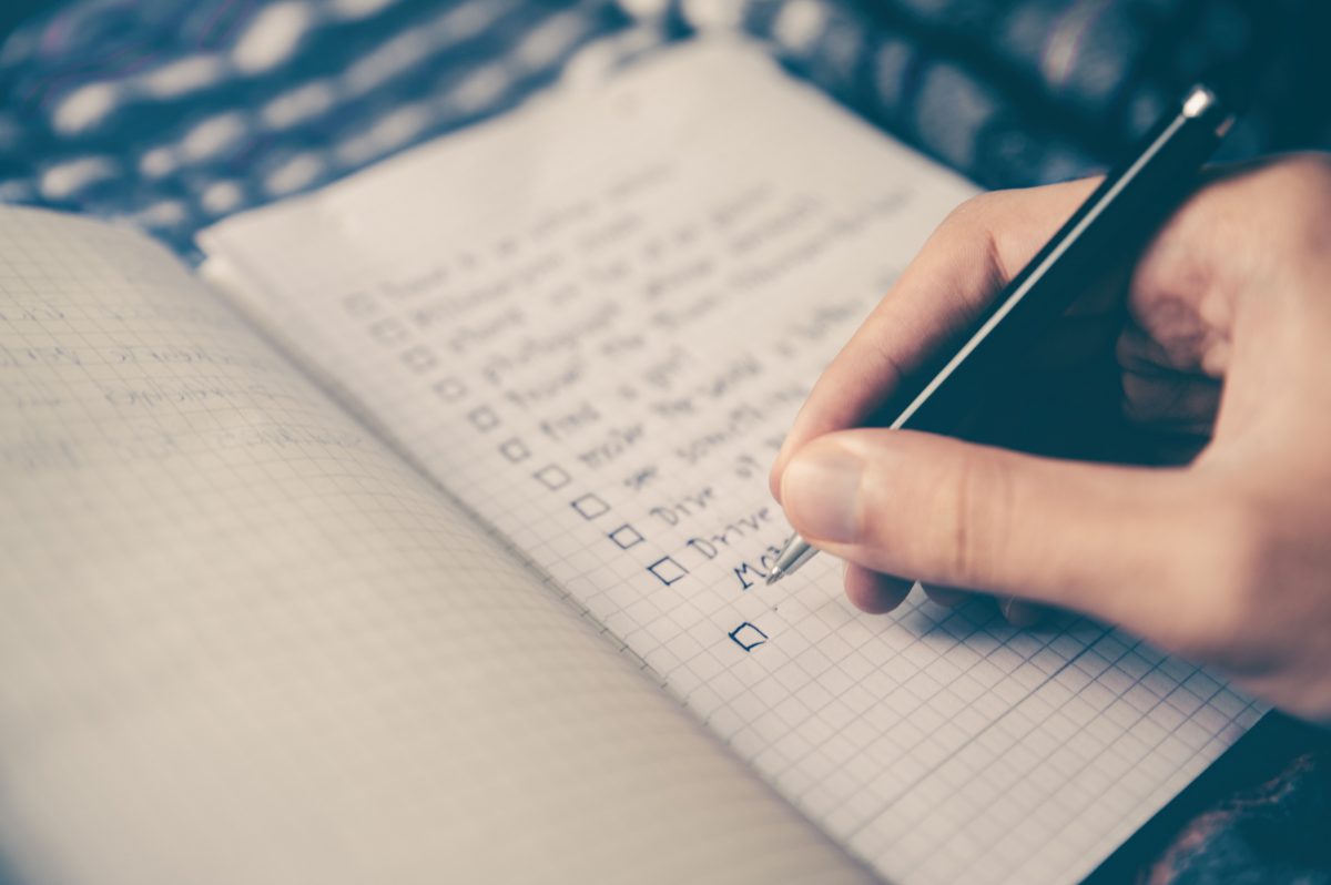 person writing checklist in notebook