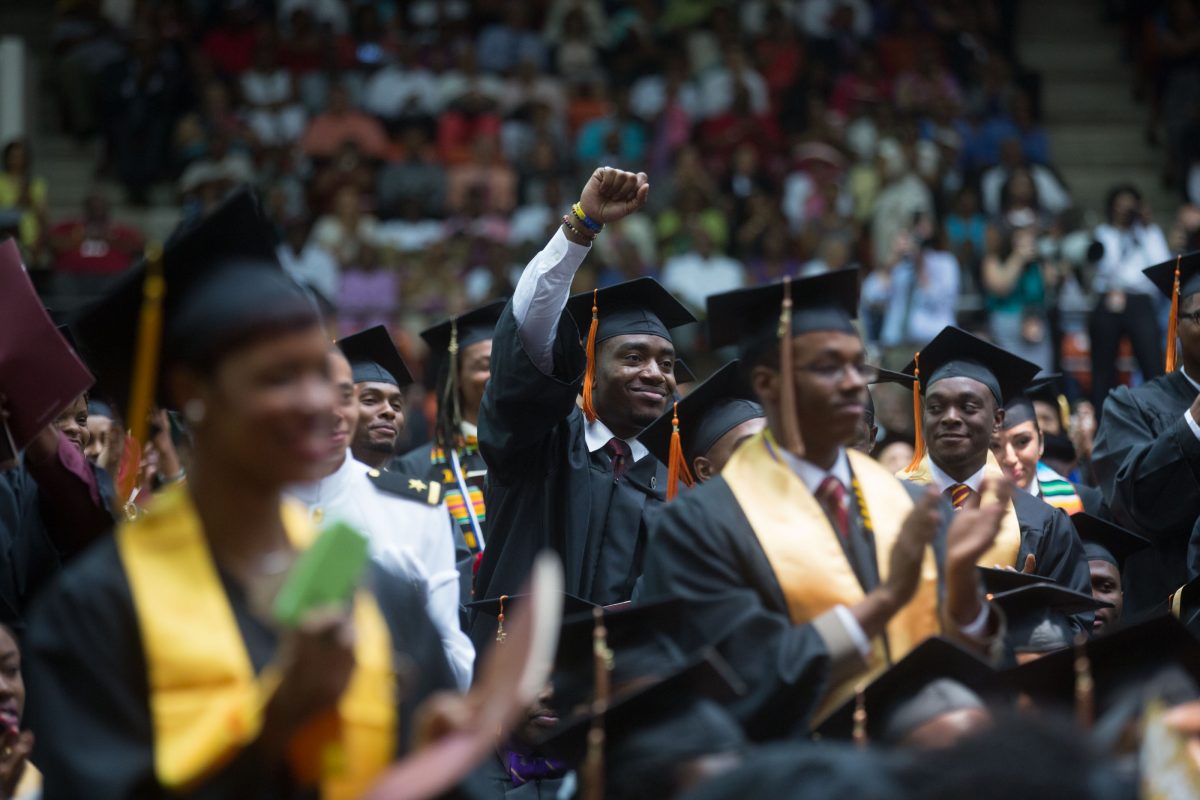 Student in graduation cap and gown lifting is fist in a sea of other graduates