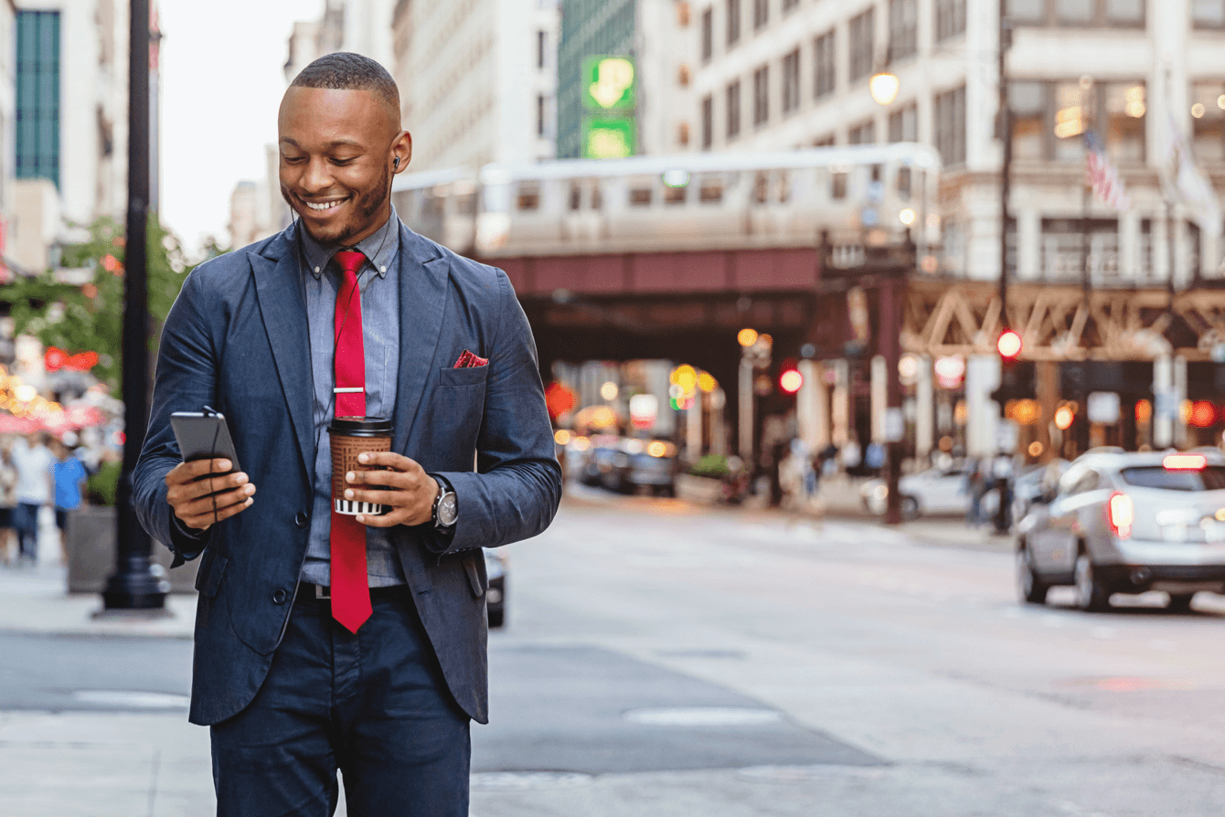 Man in suit holding coffee while smiling and looking at his phone