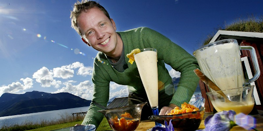 Man posing in front of food and drink with a lake and mountain behind him