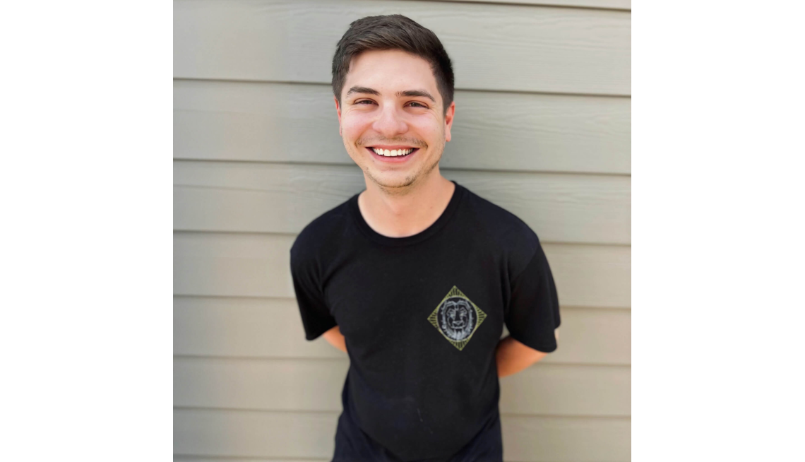 Man in a black t-shirt leans against a wall smiling.