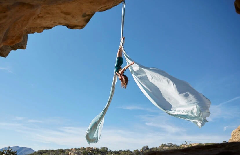 Woman practicing aerial arts. She is upside down off of the side of a cliff.