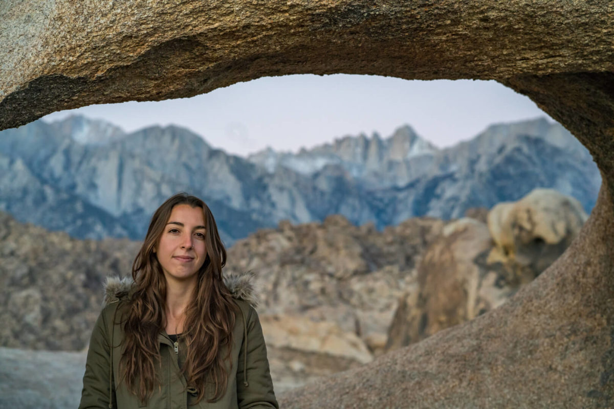 Woman with brown hair and a green jacket smiling with a mountain range in the background